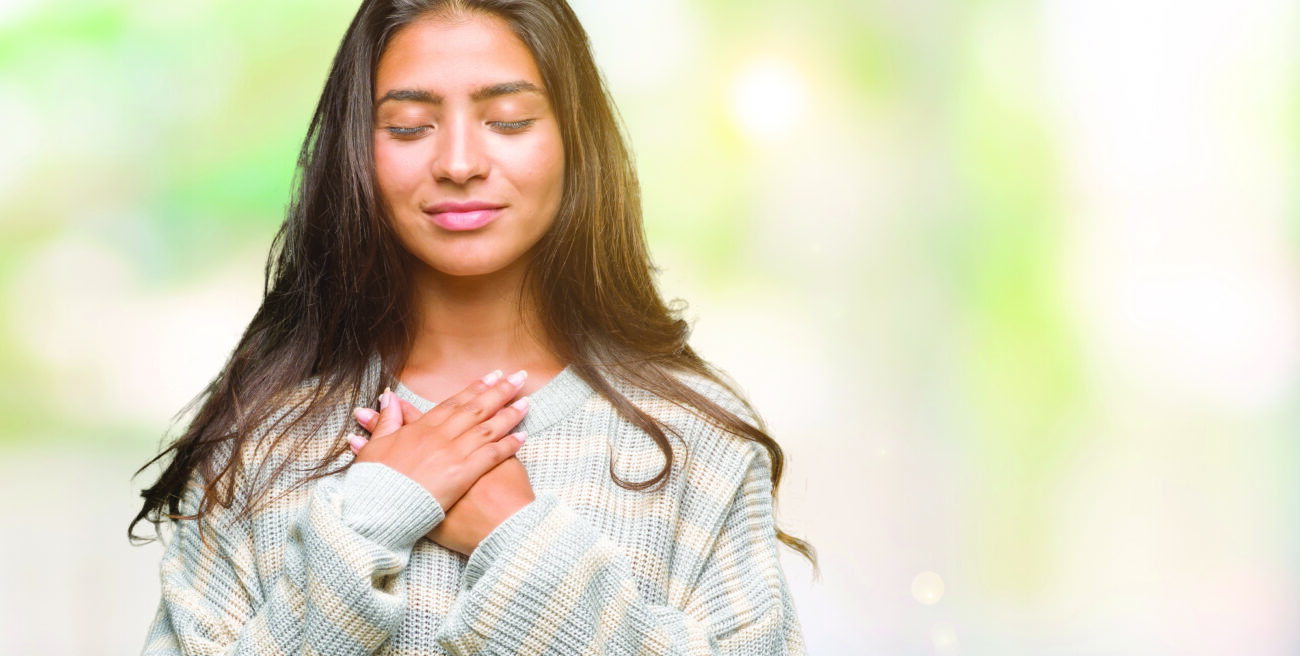 Young beautiful arab woman wearing winter sweater over isolated background smiling with hands on chest with closed eyes and grateful gesture on face. Health concept.