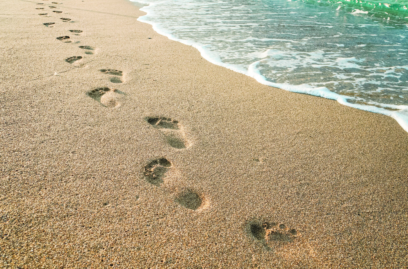 Beach, wave and footprints during the day. Texture background Footprints of human feet on the sand near the water on the beach.