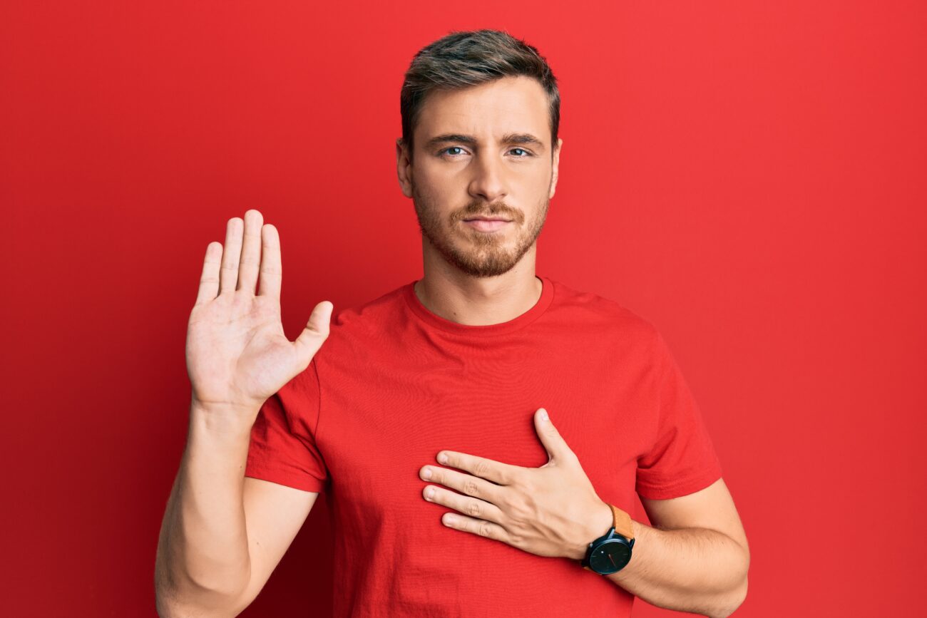 Handsome caucasian man wearing casual red tshirt swearing with hand on chest and open palm, making a loyalty promise oath