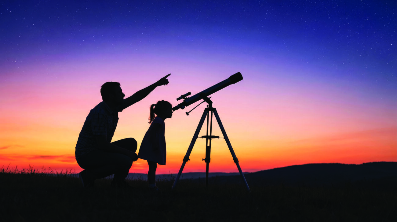 Silhouette of a father and daughter stargazing at dusk, with the child looking through a telescope and the parent pointing towards the sky during sunset. Teaching children. Space observation