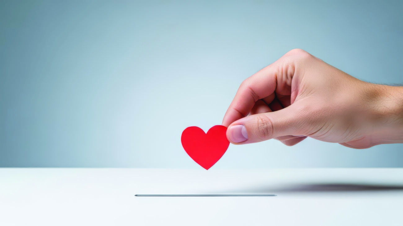 Hand dropping a small red paper heart shape into a slot or donat